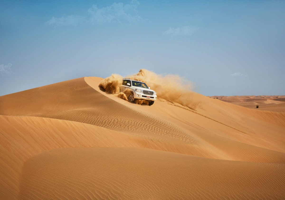 A 4x4 dune bashing amidst the golden dunes in the vast expanses of the Liwa Desert on a sunny day. crop