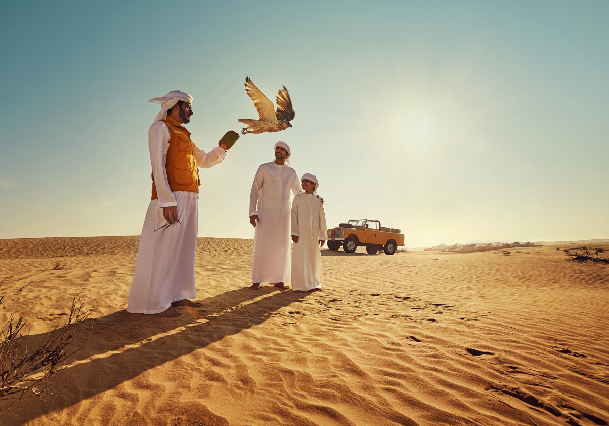 An Emirati father and son enjoying the traditional Emirati pastime of Falconry in Liwa Desert on a sunny afternoon. c